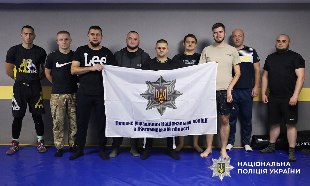 У спортивному залі учасники позують для спільного фото з прапором Головного управління Національної поліції в Житомирській області