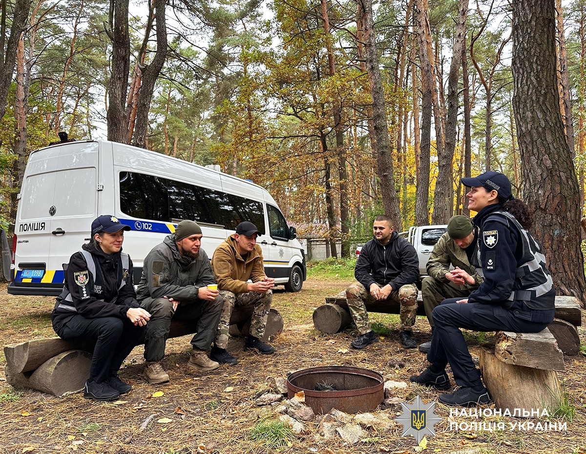 У колі на дерев’яних лавках сидять чоловіки та психологи поліції. На фоні стоїть поліцейський бус.