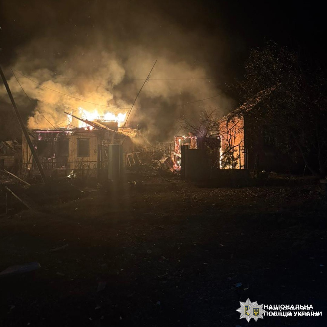 Нічна сцена в житловому районі: будівля охоплена сильним полум’ям, густий дим підіймається в небо. Яскраво-оранжеві язики вогню вириваються з даху та вікон.