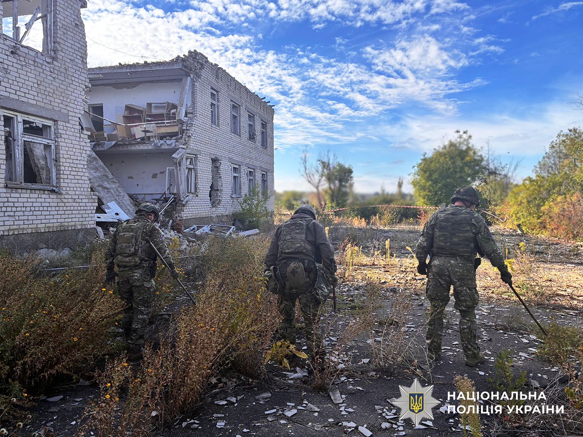 три поліцейські-вибухотехніки обстежують територію поблизу сильно пошкодженого приміщення