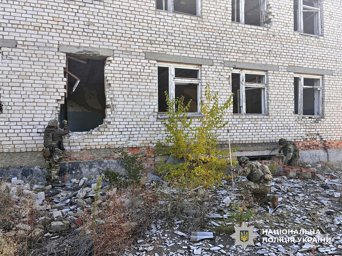 три поліцейські-вибухотехніки обстежують територію поблизу сильно пошкодженого приміщення