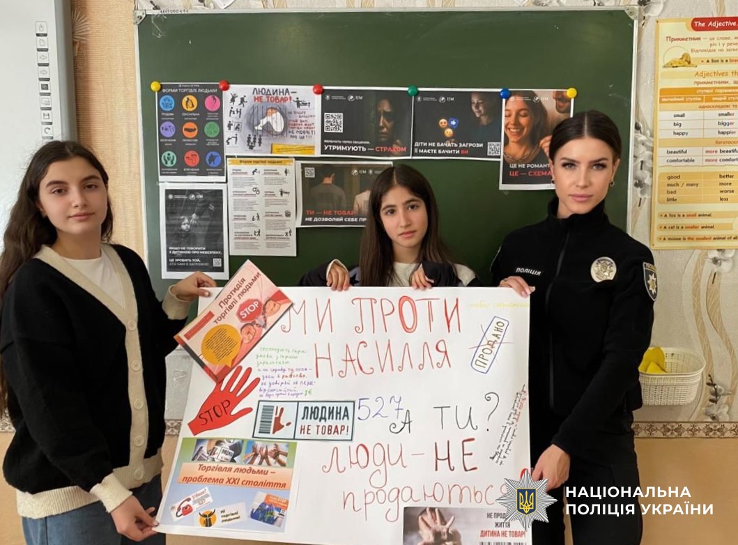 поліцейська з дітьми тримає тематичний плакат, намальований учнями