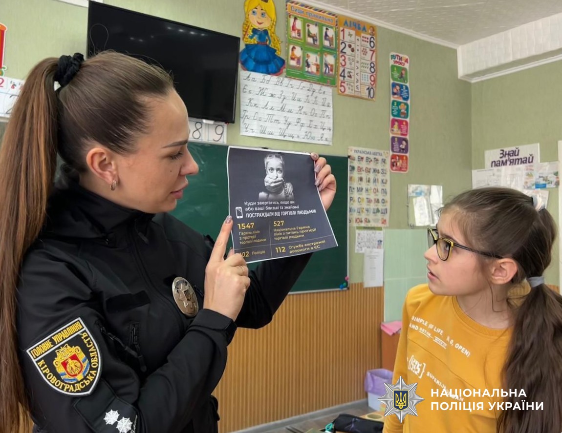 поліцейська показує учениці плакат з контактами, куди звертатися по допомогу