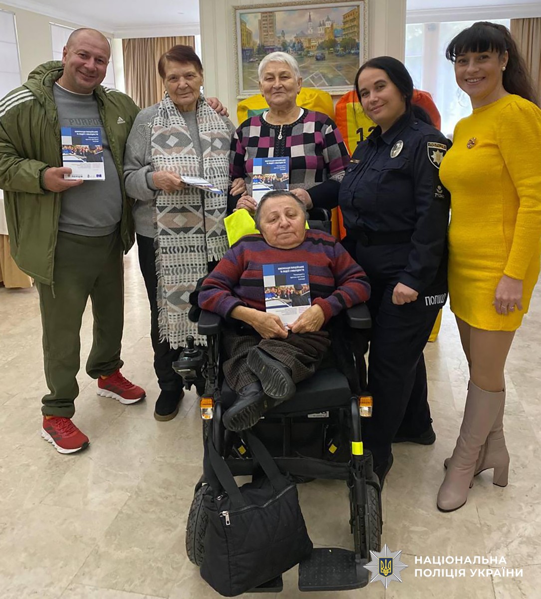 Учасники заходу: на передньому плані людина в кріслі колісному, позаду стоять п'ятеро людей