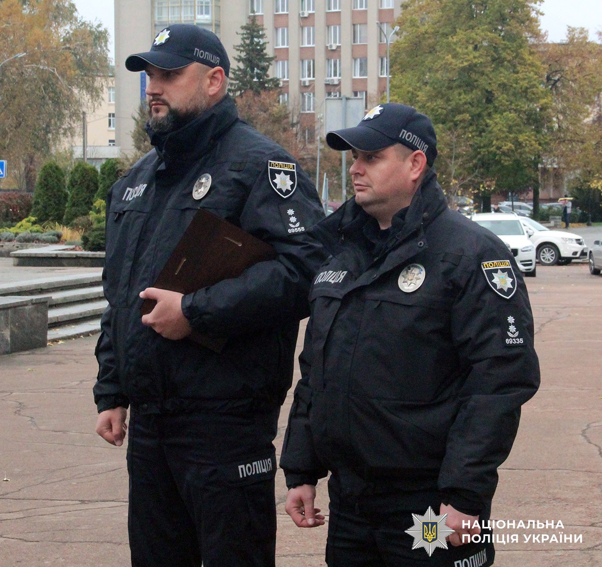 Двоє представників УГІ стоять в однострої поліцейського. Один із них тримає блокнот.