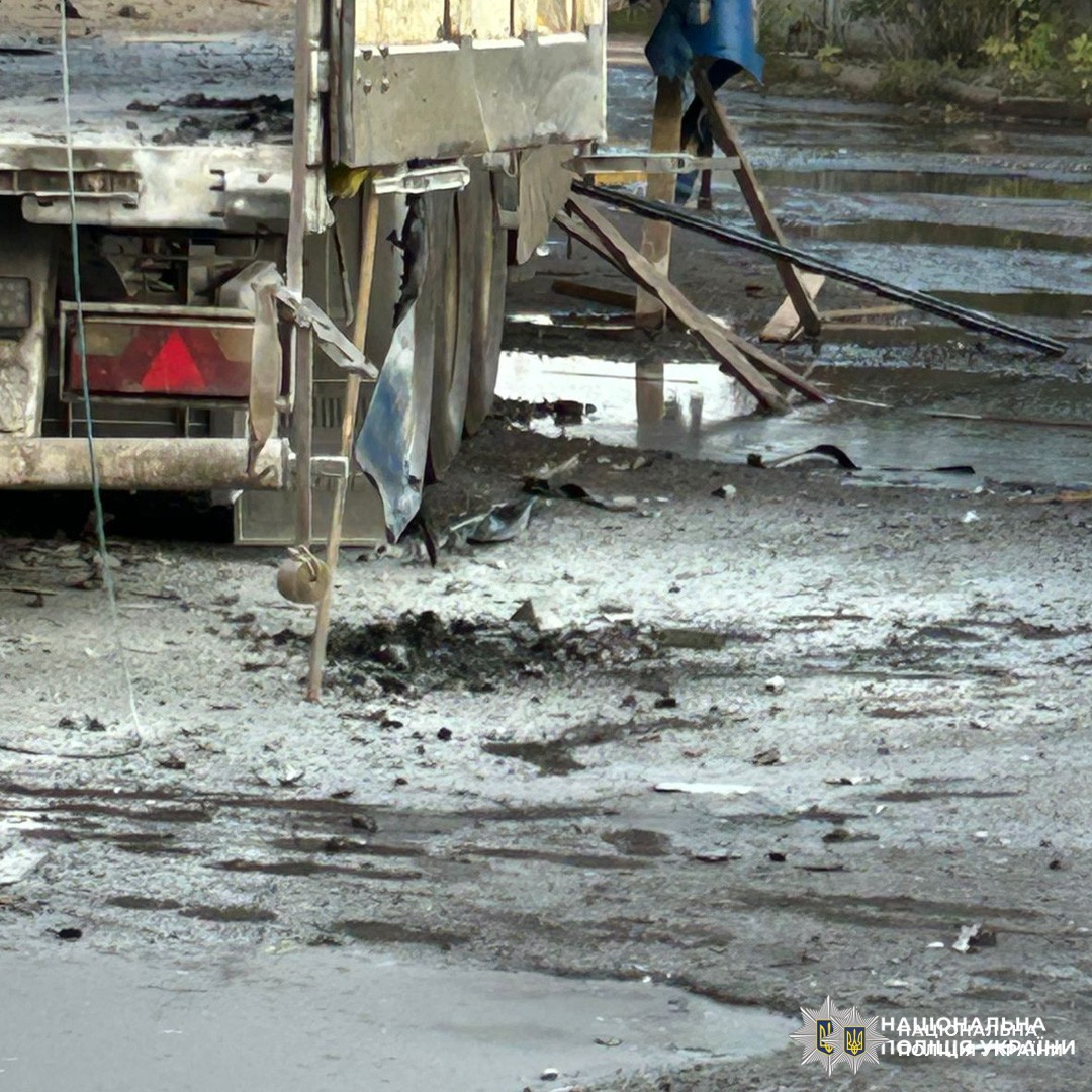 Зафіксовано пошкоджену задню частину вантажного автомобіля. Видно обірвані кабелі, фрагменти матеріалу, сліди забруднення та людину поруч.