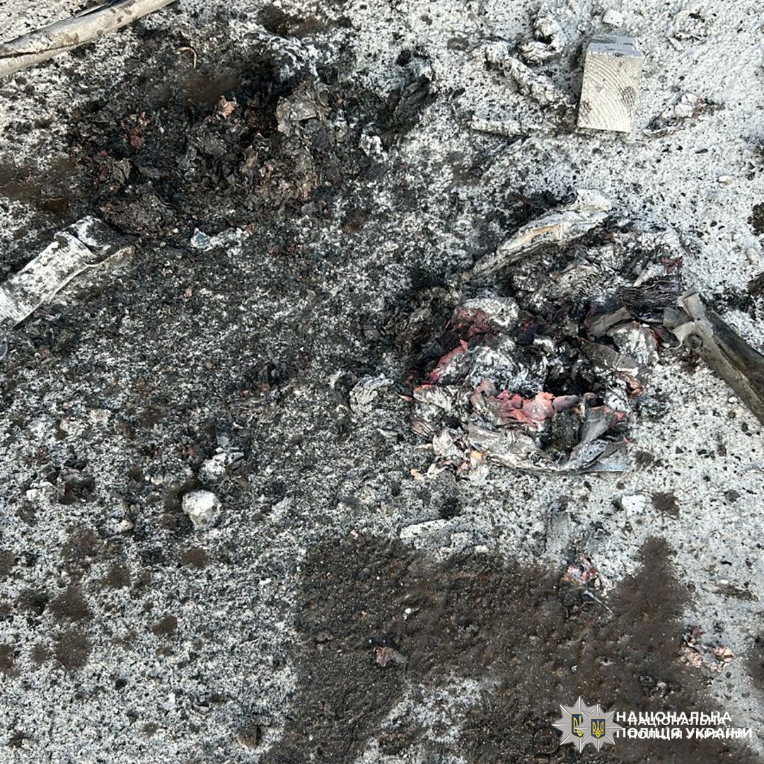 На бетонній поверхні зафіксовано сліди сильного пошкодження, ймовірно внаслідок вибуху або пожежі. Видно обвуглені ділянки, уламки металу та залишки згорілих матеріалів.