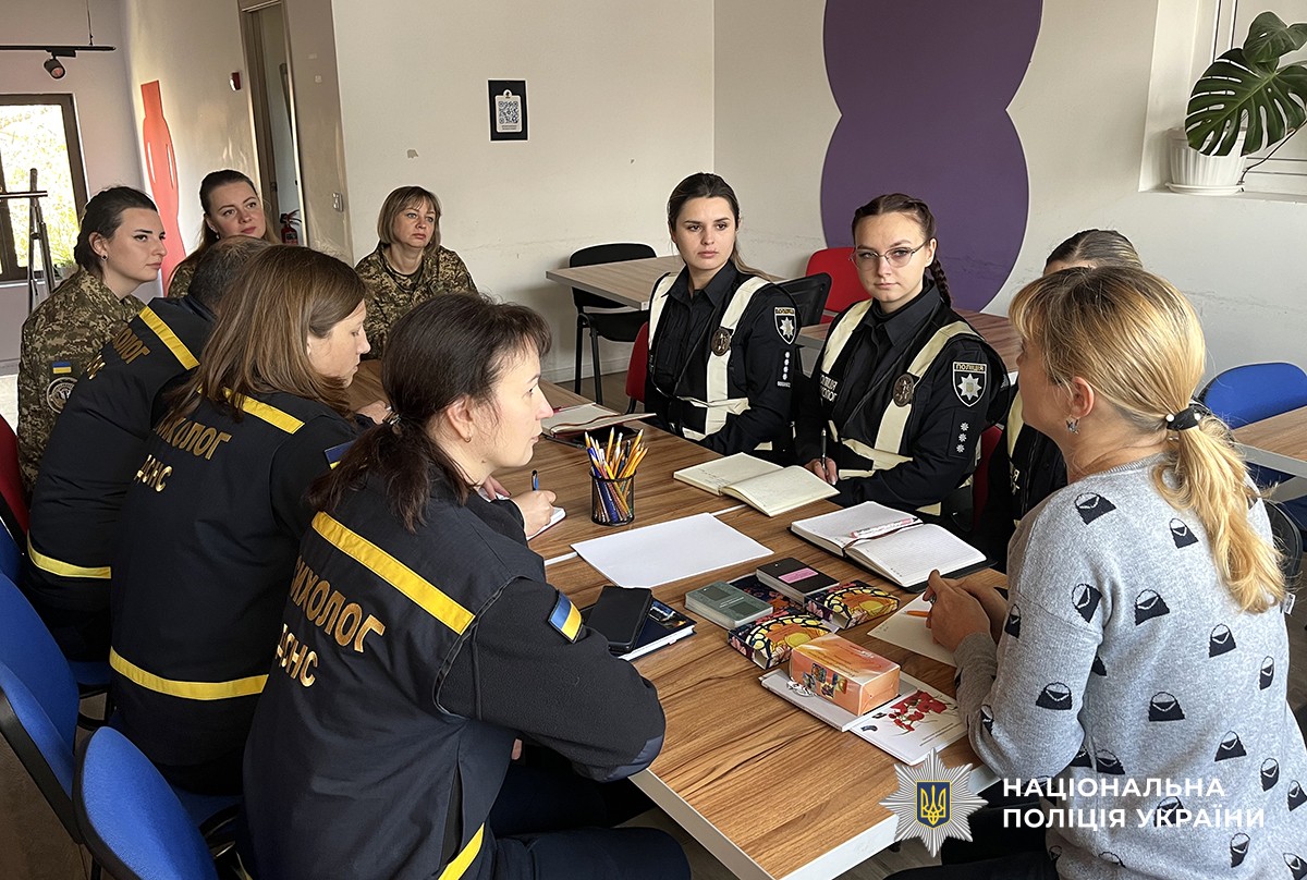 За столом у форменому одязі розташувалися психологи різних служб, уважно слухаючи психологиню, яка сидить навпроти та проводить розмову чи презентацію.