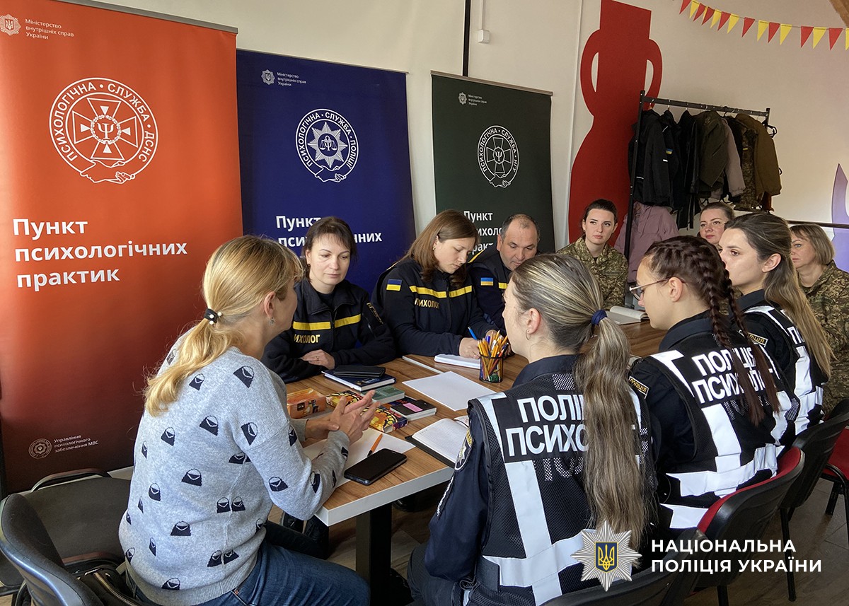За столом у форменому одязі розташувалися психологи різних служб, уважно слухаючи психологиню, яка сидить навпроти та проводить розмову чи презентацію. Представниця ДСНС щось записує у блокноті.