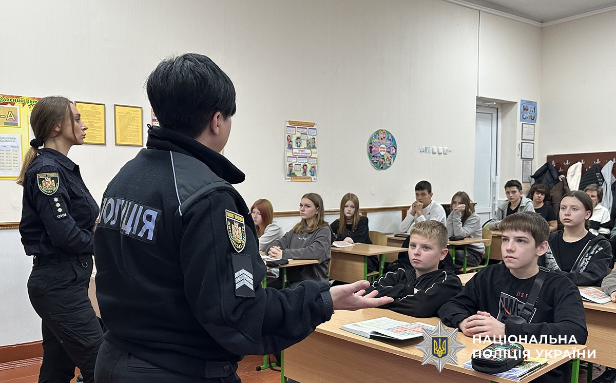 Учні сидять за партами, перед ними стоять дві поліцейські в однострої, одна з них щось розповідає учням.