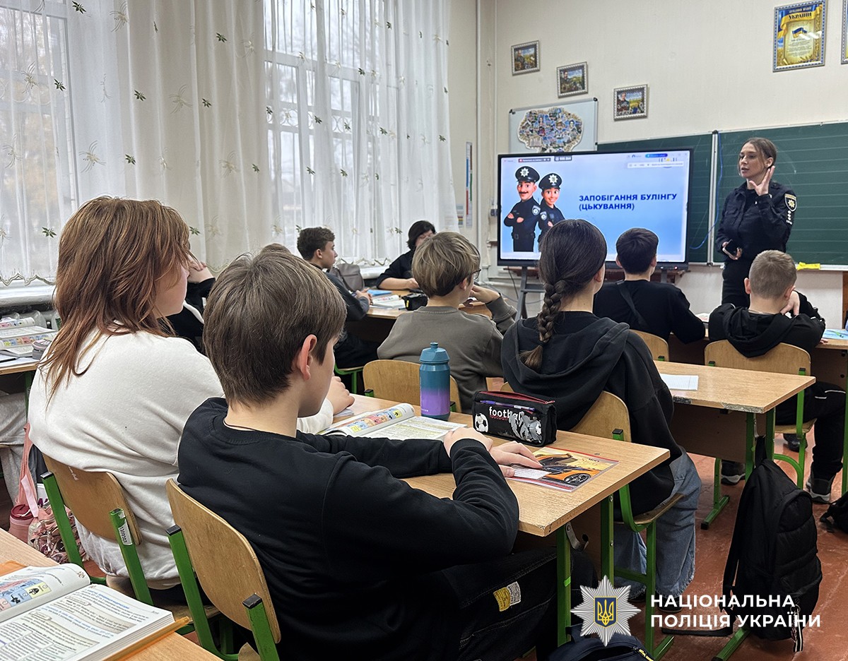 Учні сидять за партами, на задньому плані демонструється слайд із текстом про булінг та поліцейська щось розповідає.