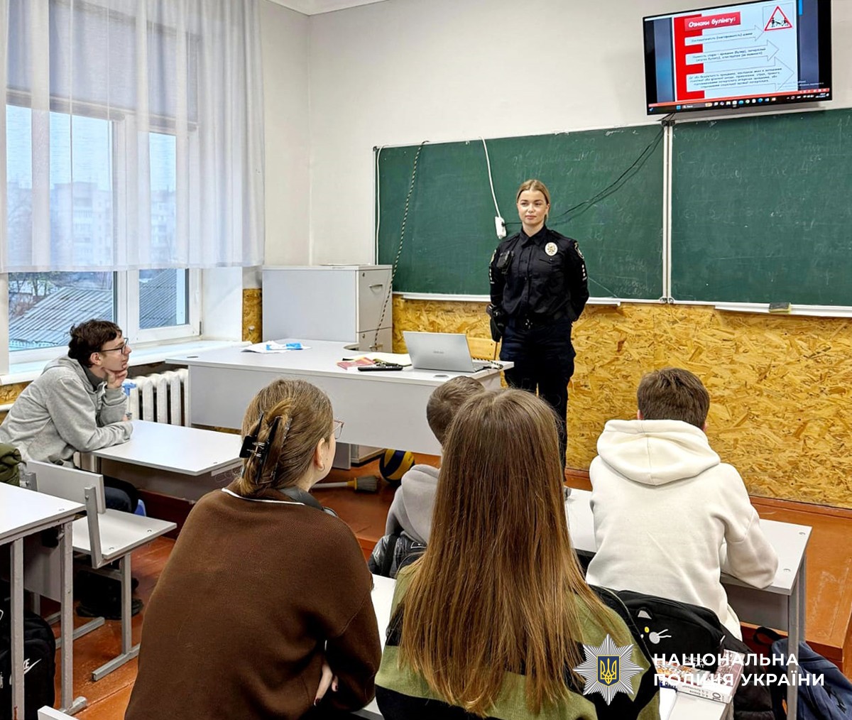 В шкільному класі біля дошки стоїть поліцейська, учні сидять за партами.