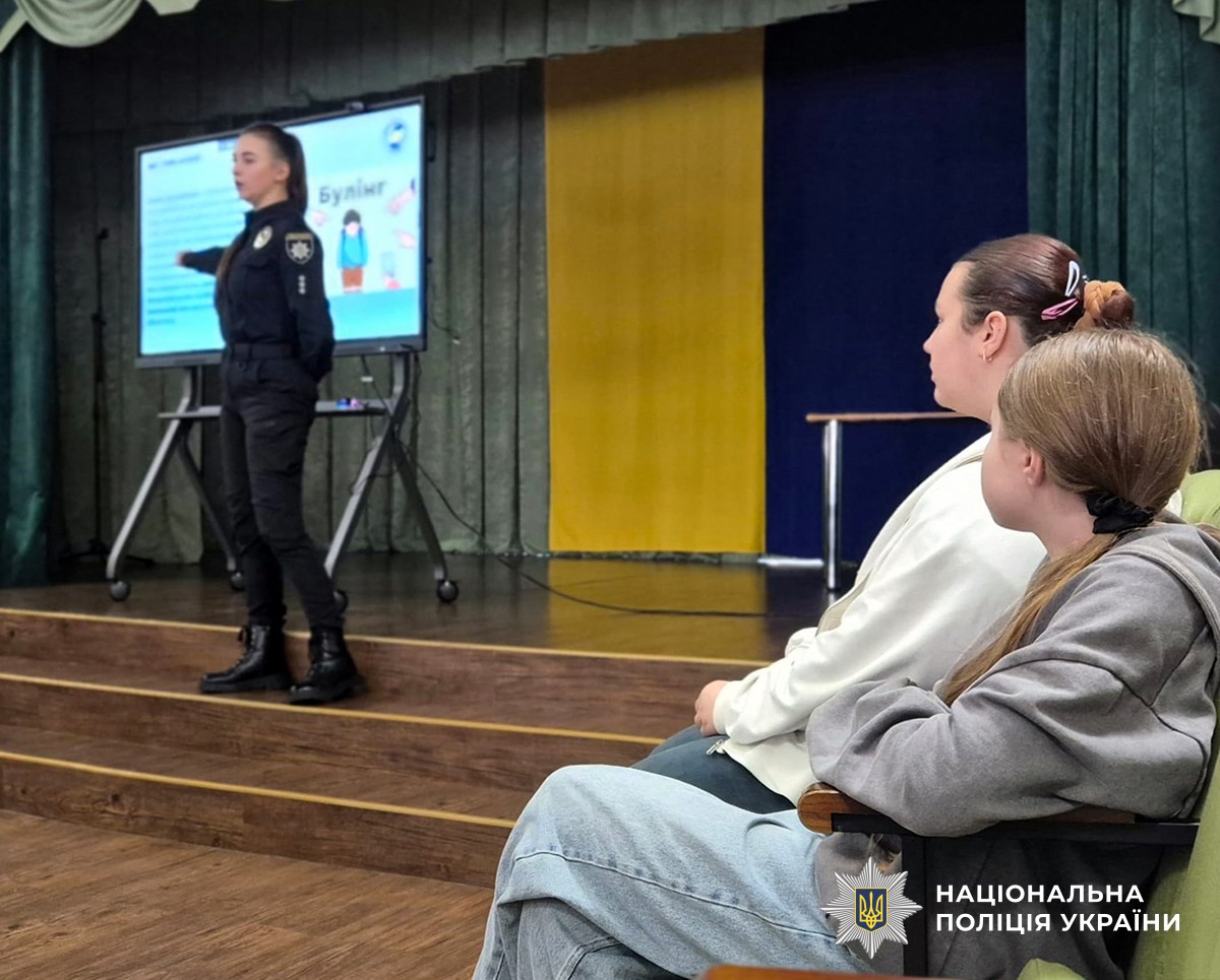 В актовому залі дві ліцеїстки уважно слухають поліцейську, яка під час виступу показує рукою на слайд презентації, присвяченої темі булінгу.