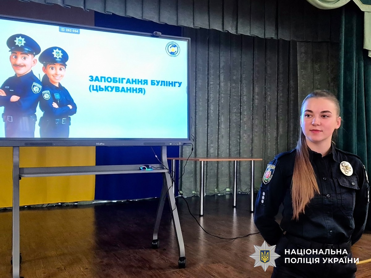 Поліцейська в актовій залі. На задньому плані демонстрація презентації "запобігання булінгу (цькування)"