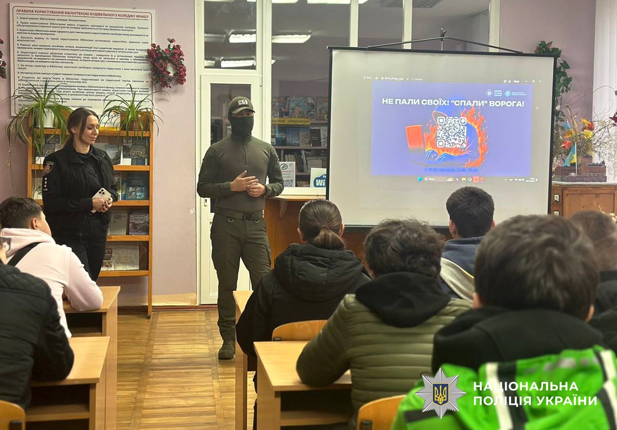 Поліцейська та представника СБУ, які стоять у центрі аудиторії перед першокурсниками. Поруч із ними на екрані демонструється презентація, присвячена темі вербування.