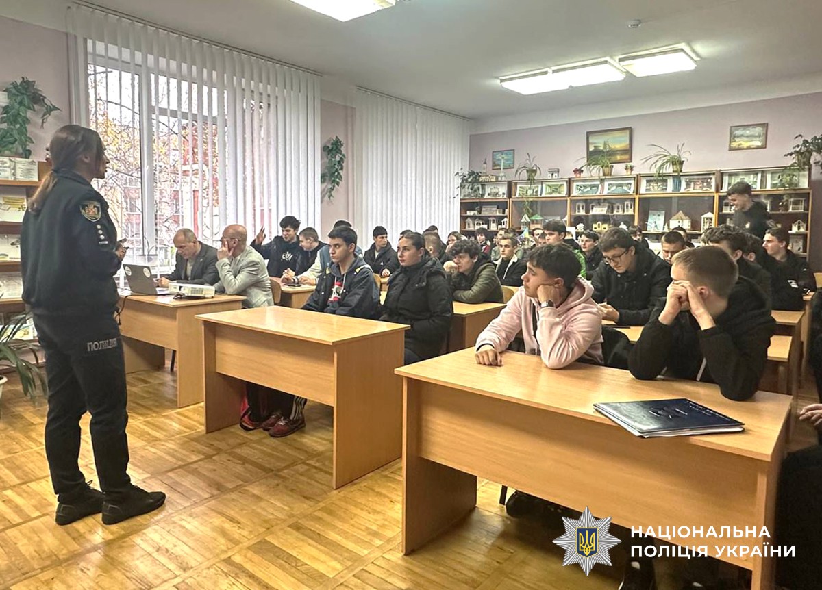 Першокурсники сидять за партами перед ними стоїть поліцейська.