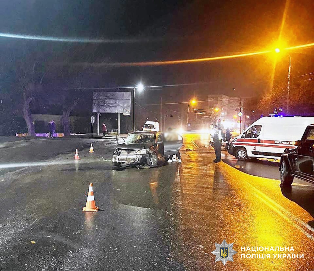 Дорога, освітлена вуличними ліхтарями, посередині пошкоджений в ДТП автомобіль, збоку - машина швидкої допомоги