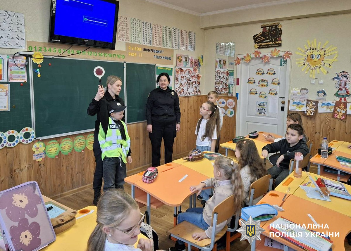 Дві поліцейських проводять заняття для учнів у ліцеї. на одному з хлопчиків одягнутий жилет, а в руках - поліцейський жезл