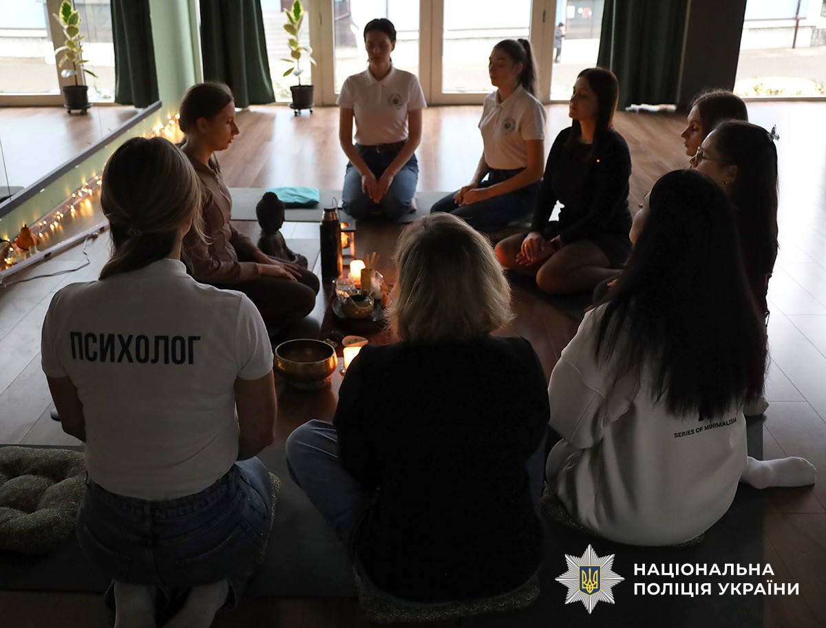 Люди сидять у колі з закритими очима на підлозі зі свічками, створюючи спокійну, медитативну атмосферу.