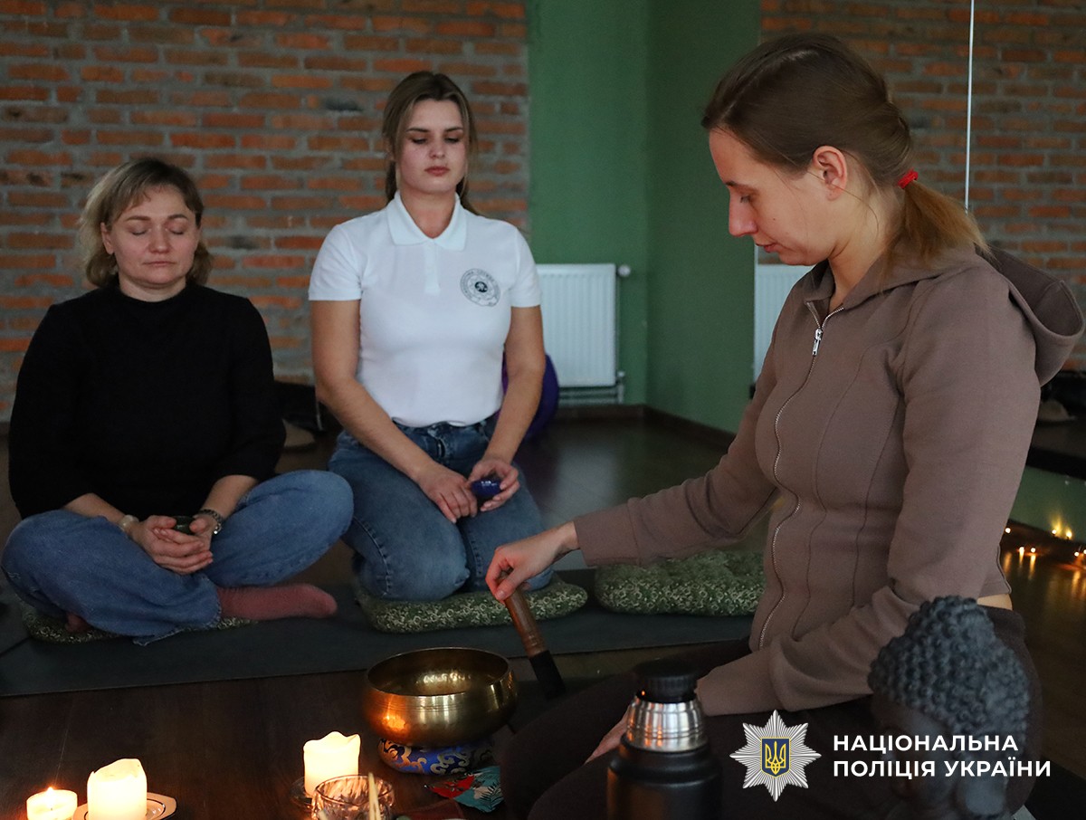 Три жінки зосереджено медитують біля свічок, одна з них використовує співочу чашу.