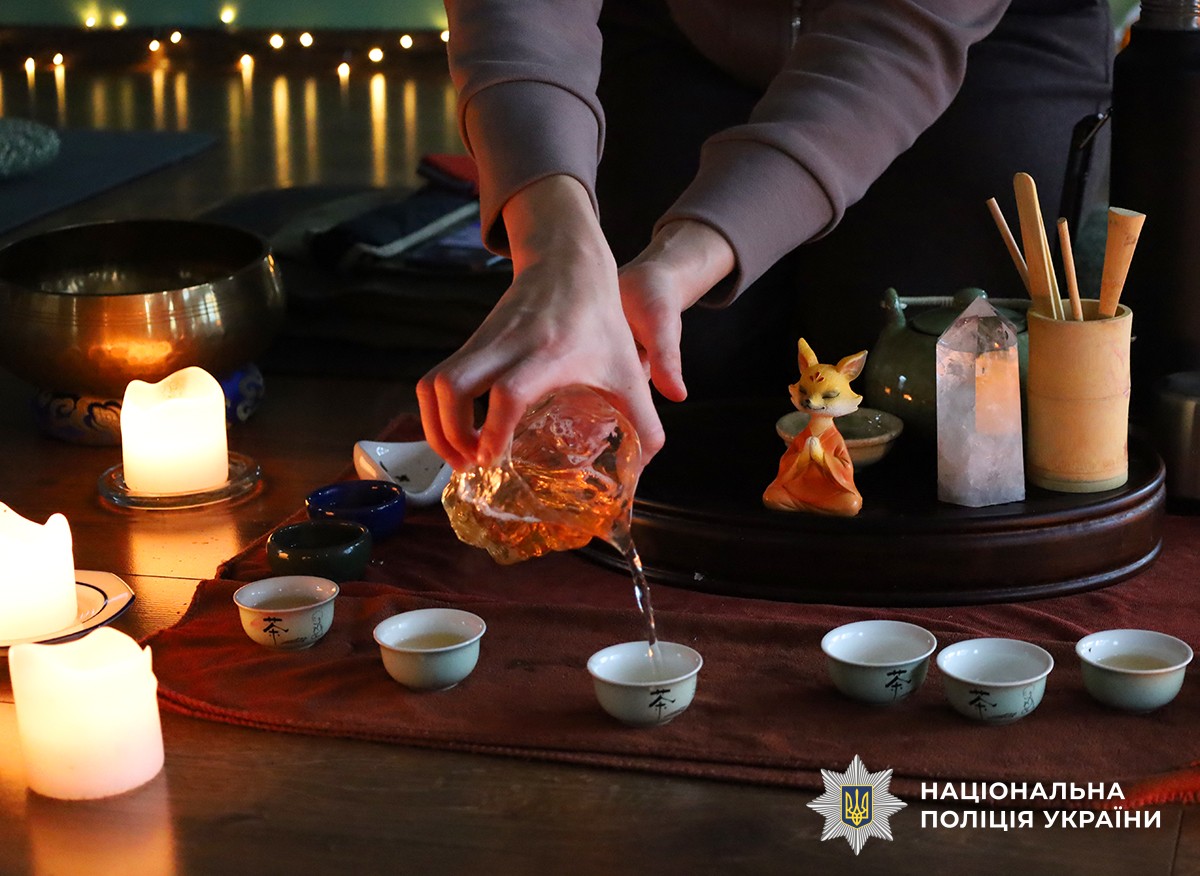 На підлозі маленьки посудики в які жіночі руки які наливають чай зі стаканчика прозорого.