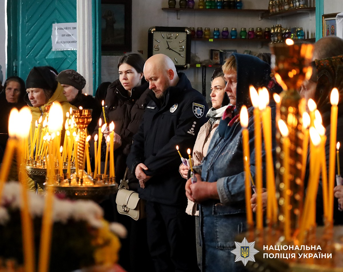 У церкві люди з запаленими свічками стоять на поминальній службі. Усі схилили голови в молитві.