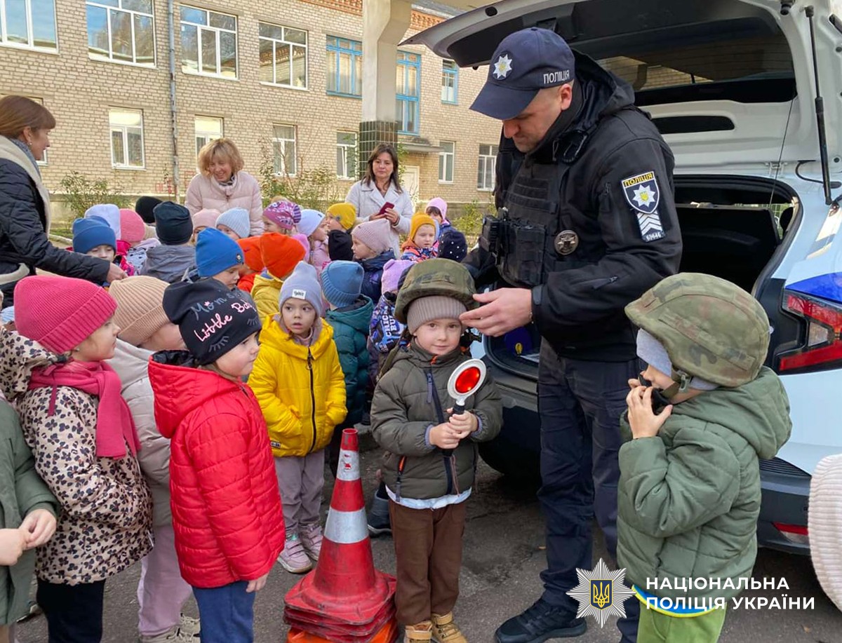 Поліцейський приміряє шолом дитині поблизу службового автомобіля