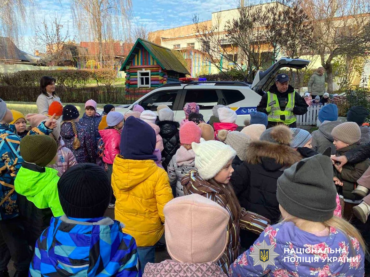 Поліцейський поблизу службового автомобіля проводить заняття для дітей