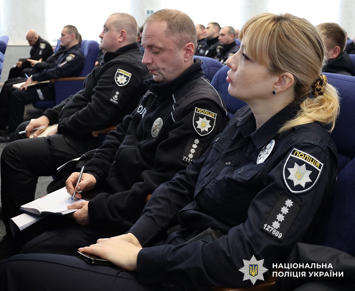 Поліцейські сидять в актовому залі на синіх стільцях, один із них робить запис у блокноті.