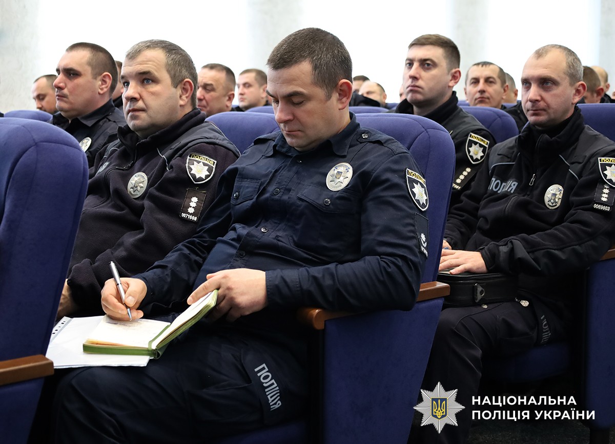 Поліцейські сидять в актовому залі на синіх стільцях, один із них робить запис у блокноті.