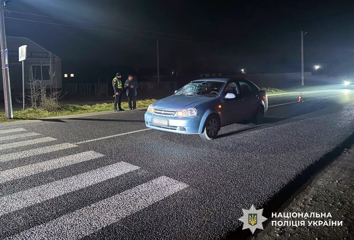 Легковий автомобіль стоїть перед пішохідним переходом на дорозі, поруч на узбіччі - поліцейський та чоловік в цивільному одязі