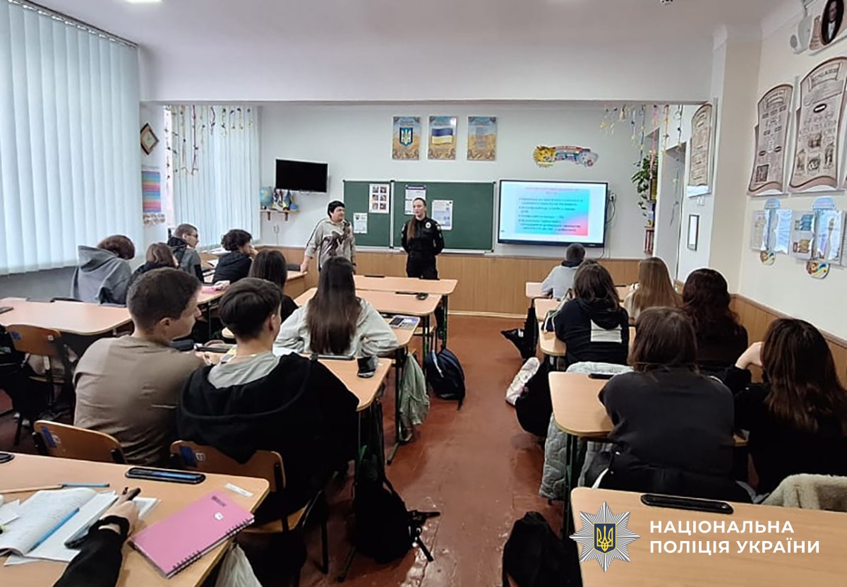 У класі за партами сидять діти та слухають поліцейську та працівницю соцслужби
