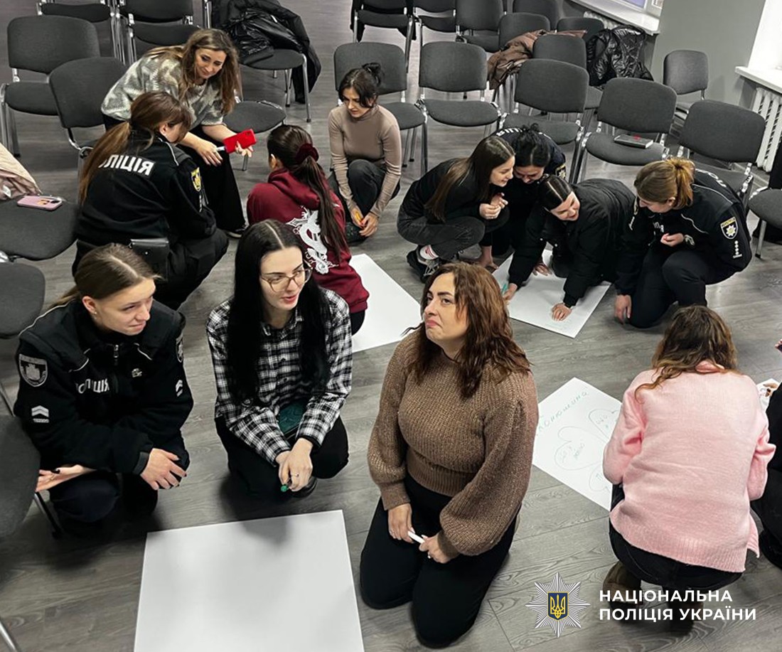 В актовому залі, на підложі сидять жінки та щось пишуть на ватманах.