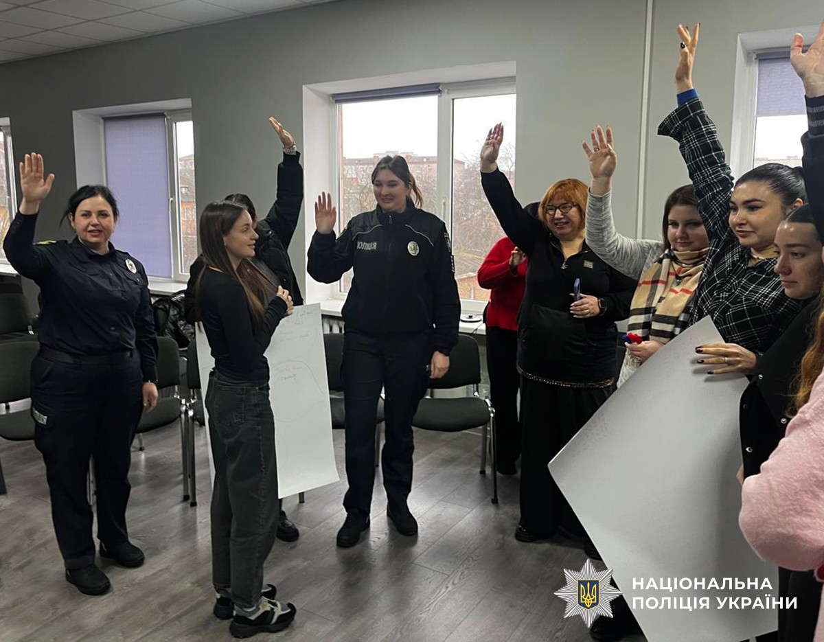 В актовому залі стоять жінки. Двоє з них з ватманами в руках. Усі жінки підінмають руку до гори.