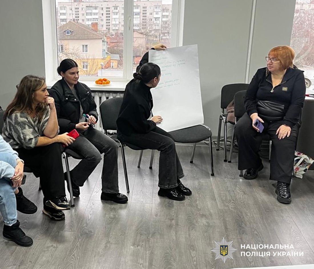 У напівколі, на стільцях сидять жінки да дивляться як одна з них роз'яснює те, що написано на ватмані.