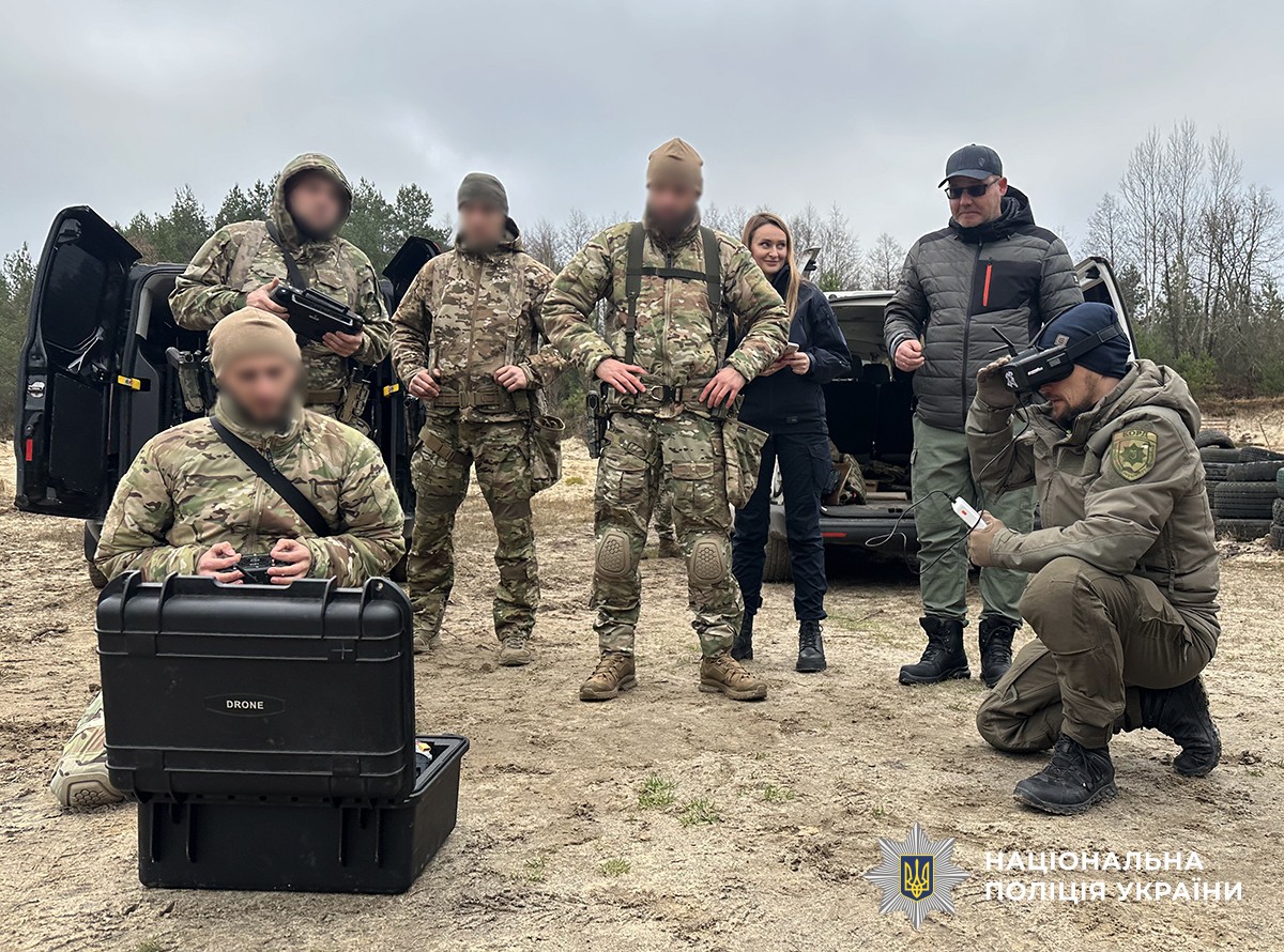 Поліцейські у військовій та тактичній формі на полігоні. Дехто тримає обладнання для керування дроном, один з чоловіків сидить перед кейсом із написом «DRONE». Ще один учасник у тактичній формі тестує окуляри або шолом для FPV-керування.