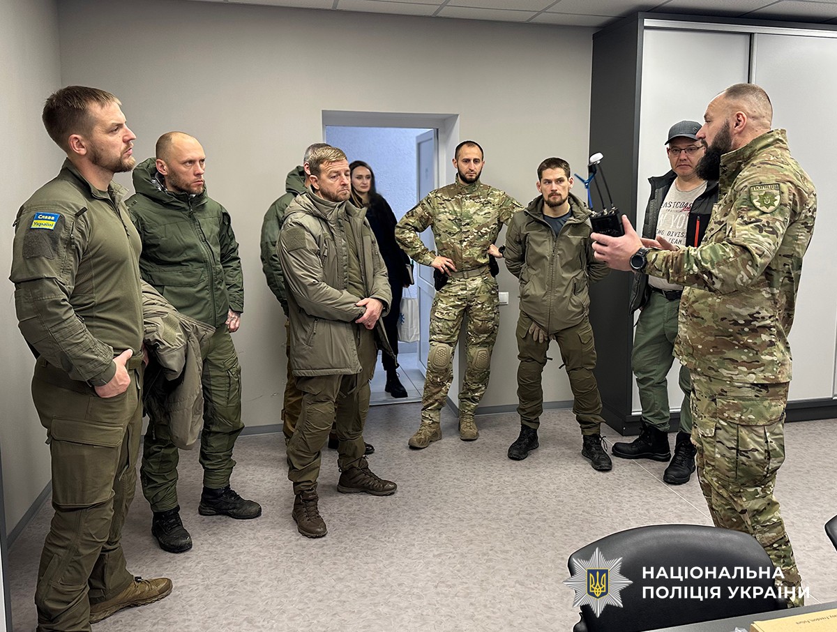 У кабінеті перебувають поліцейські у військовій та тактичній формі. Один із них тримає у руках прилад і щось пояснює, а інші уважно слухають.