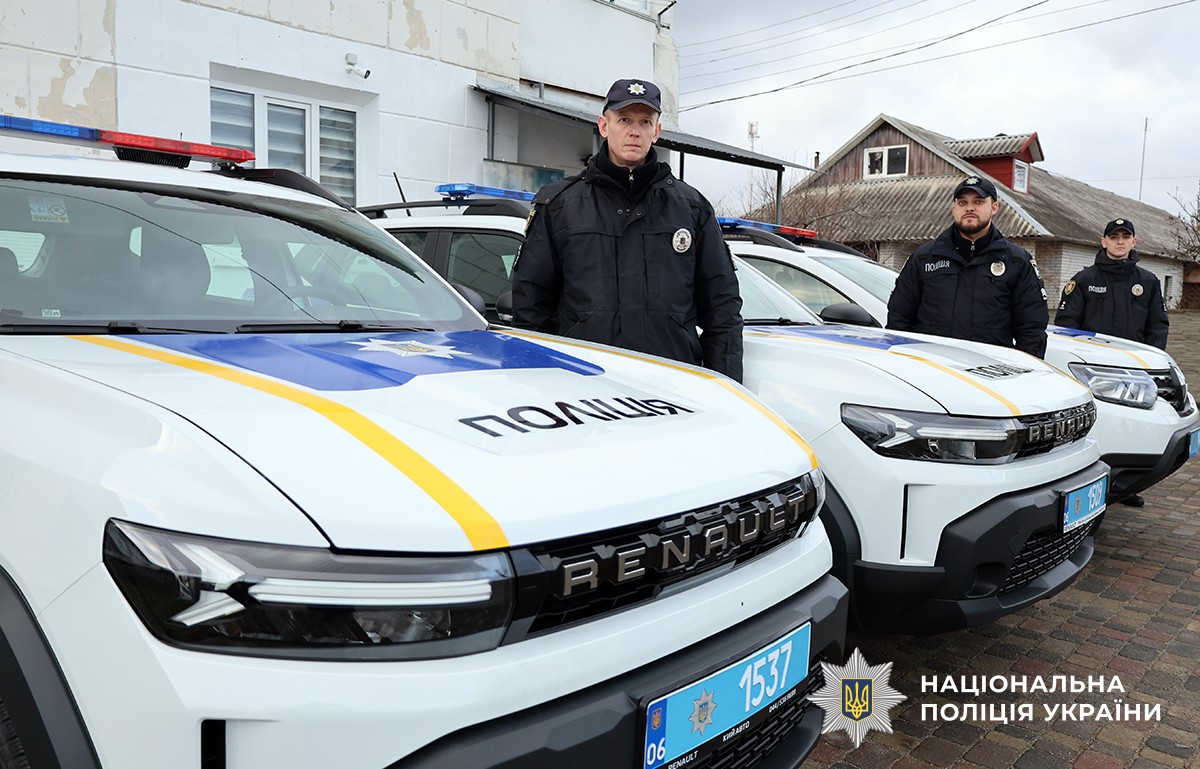 Троє поліцейьских стоять біля поліцейських автомобілів.