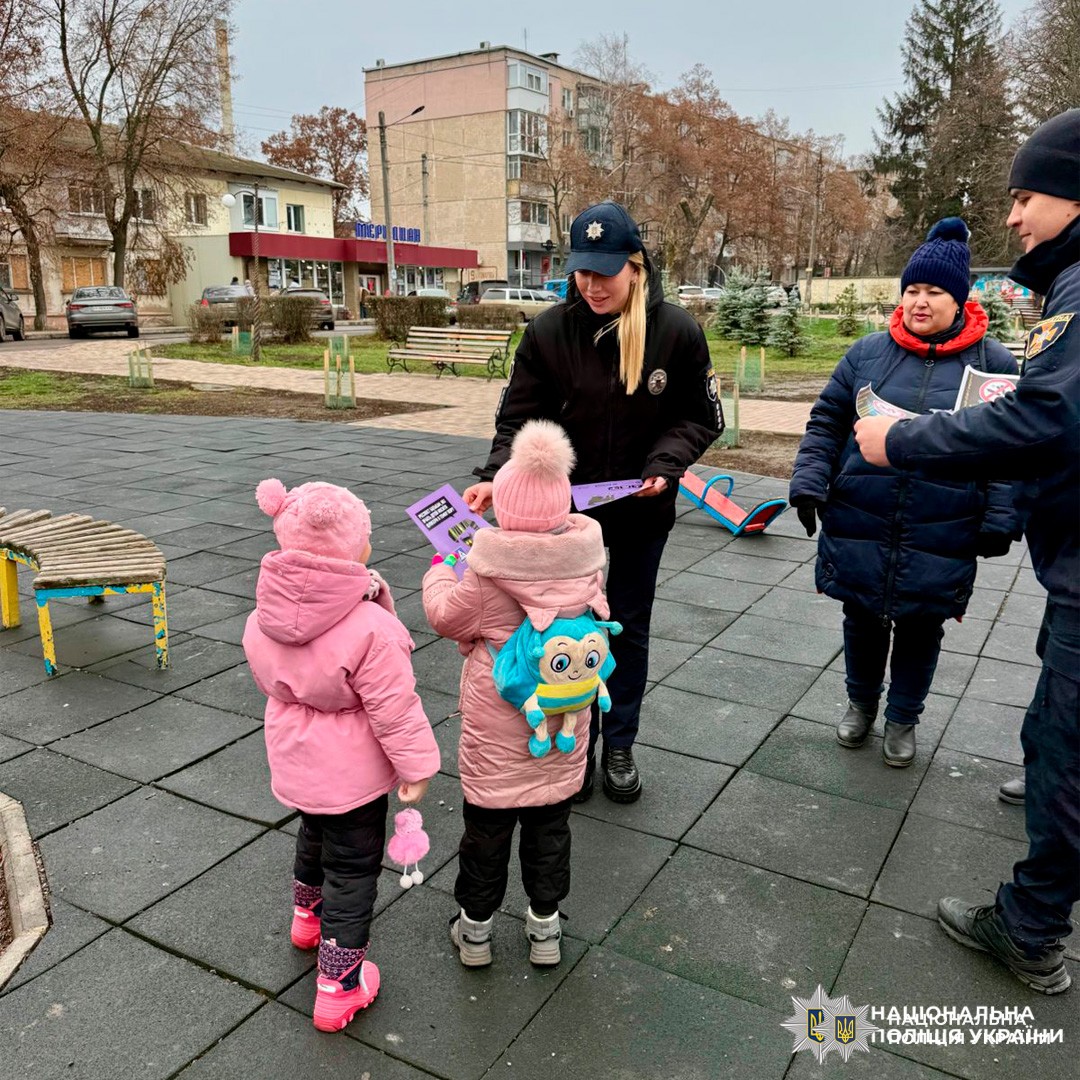 Поліцейські спілкуються з дітьми на дитячому майданчику, роздаючи інформаційні матеріали.