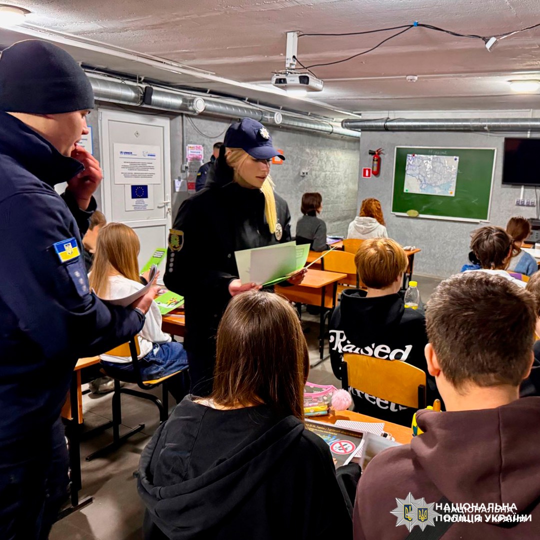 Поліцейські проводять заняття з безпеки для учнів у класі з елементами укриття.
Один із поліцейських роздає учням інформаційні матеріали.