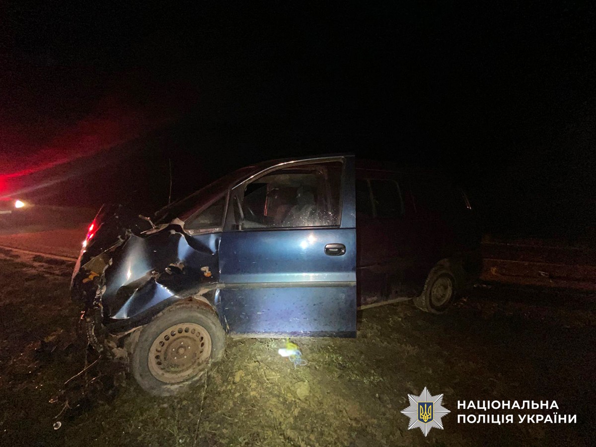 легковий автомобіль з сильно пошкодженою передньою частиною стоїть на узбіччі, відчинені двері, навколо уламки, освітлення від фар.