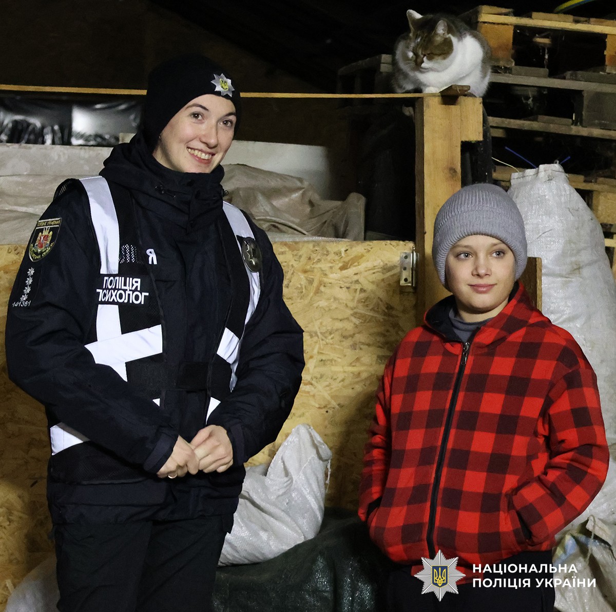 Хлопчик у червоній куртці поруч із ним стоїть поліцейська у стайні.