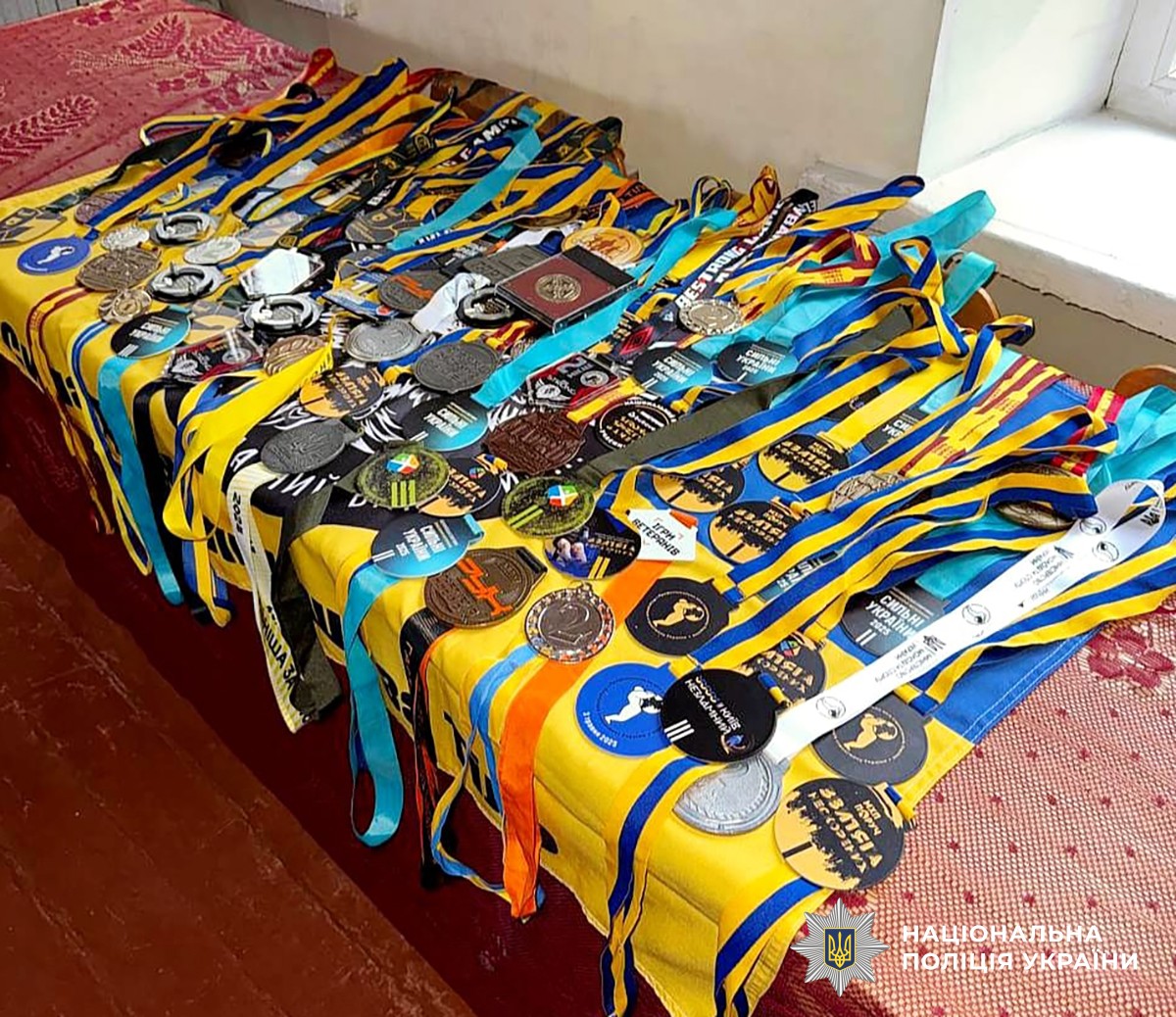 десятки медалей лежать на столі на жовто-блакитному прапорі