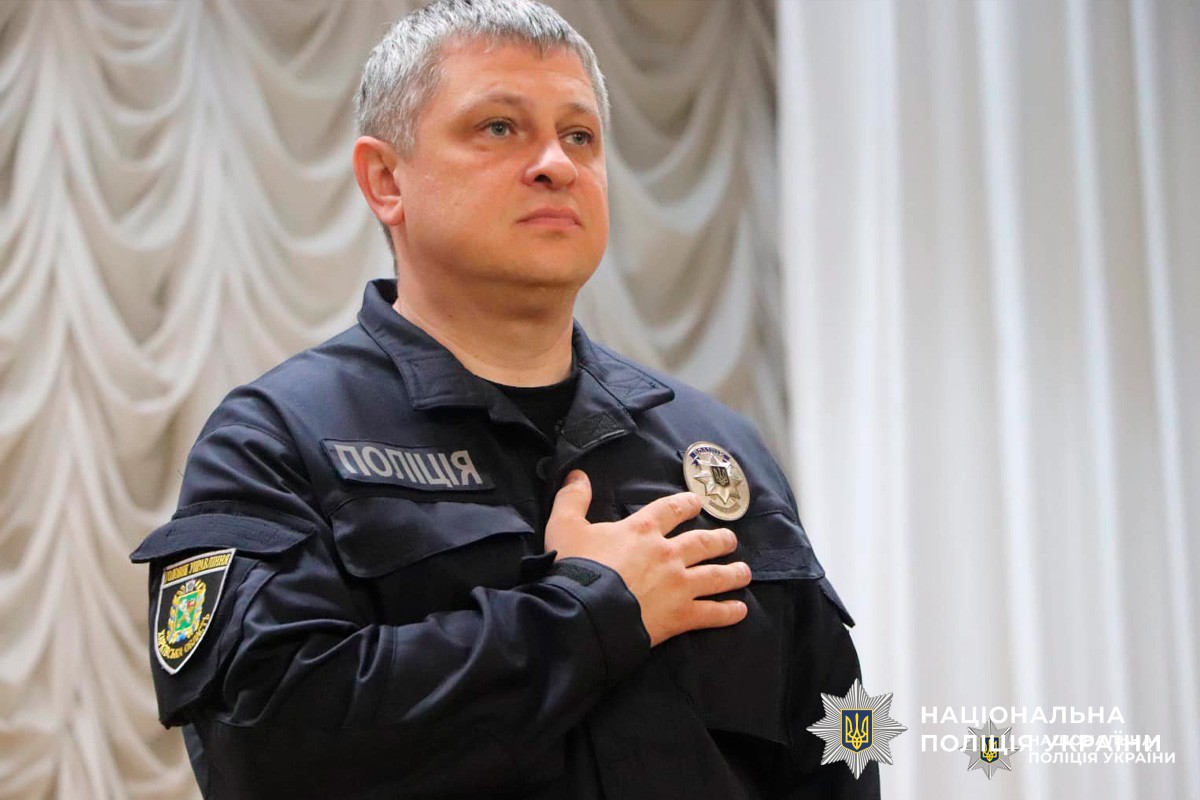 Офіцер Національної поліції України стоїть у формі з рукою на серці.