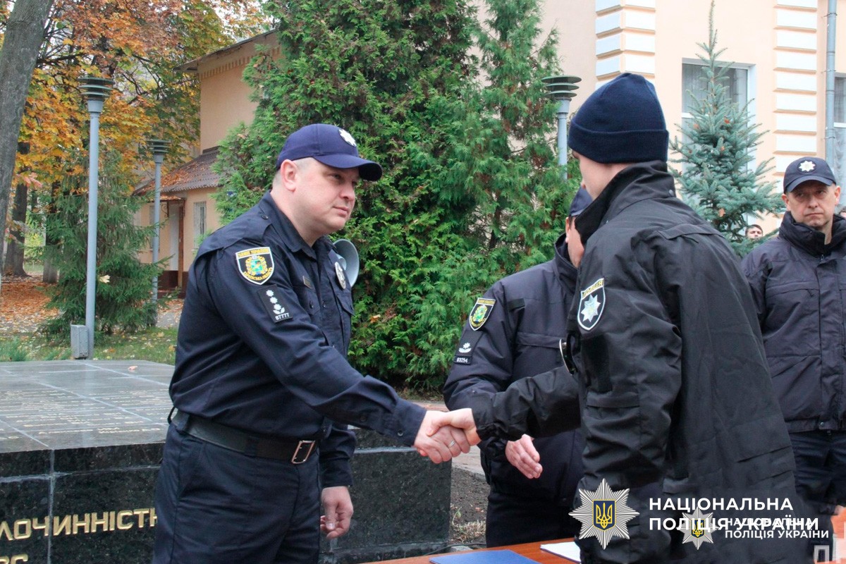 Двоє офіцерів Національної поліції України тиснуть руки під час урочистої події на відкритому повітрі.