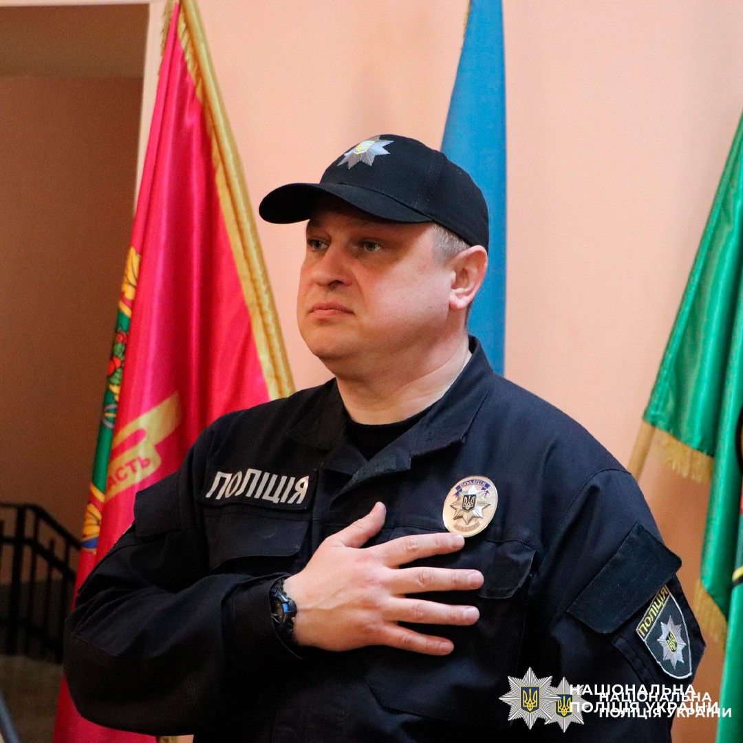 Офіцер Національної поліції України стоїть у формі з рукою на серці.