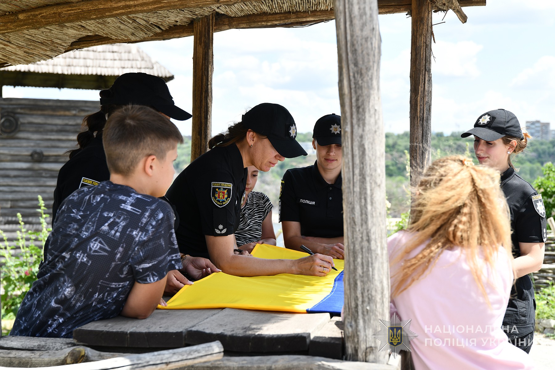 Поліцейські служби освітньої безпеки разом з дітьми підписують прапор на Запорізькій Січі. Липень 2025 року.
