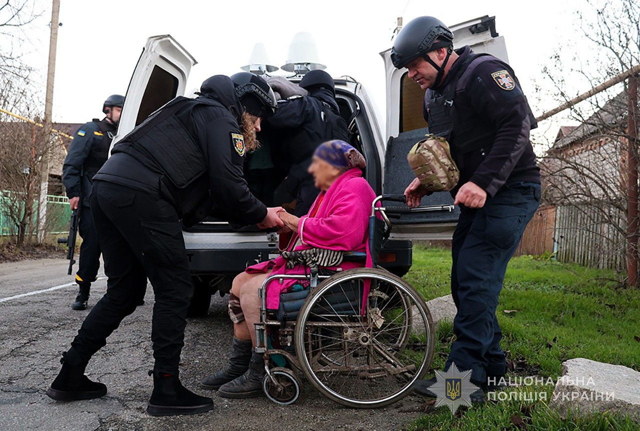 Поліцейська підбадьорює маломобільну жінку, яка залишає свою домівку. Евакуаційні заходи в селі Малокатеринівка. Грудень 2025 року.