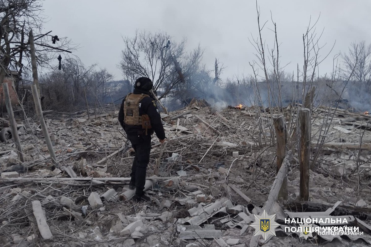 Співробітник Національної поліції України оглядає місце руйнувань після вибуху, серед уламків та диму.