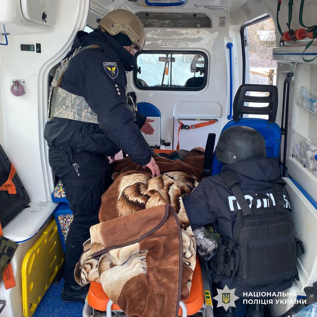 Поліцейські у тактичному спорядженні надають допомогу постраждалому в кареті швидкої.